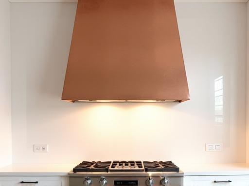 En specialdesignad köksfläkt i hamrad koppar monterad över en modern spis.